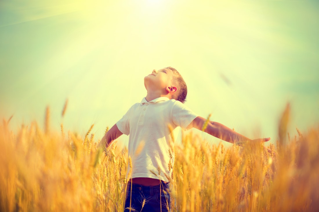 Ein Junge steht mit ausgebreiteten Armen in einem sonnenbeschienenen Kornfeld